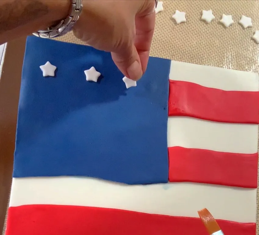 Hand placing white fondant stars on the blue field.