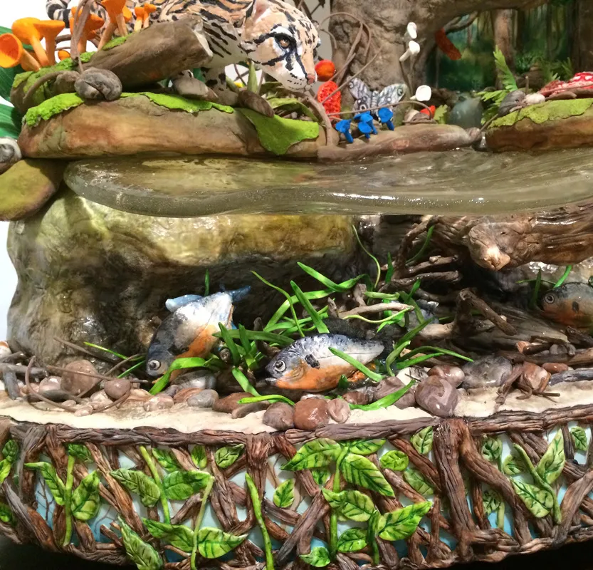A sculpted cake showing a jaguar on a rocky outcrop above a stream with fish, surrounded by mushrooms and moss.