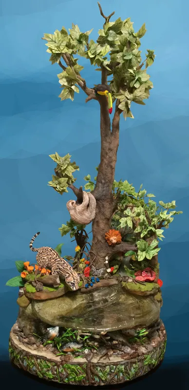 A sculpted cake depicting an Amazon rainforest scene with a toucan, sloth, and jaguar around a stream.