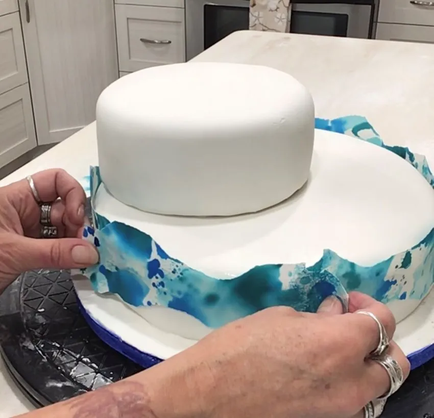 Applying colored paper strips to the lower cake tier.