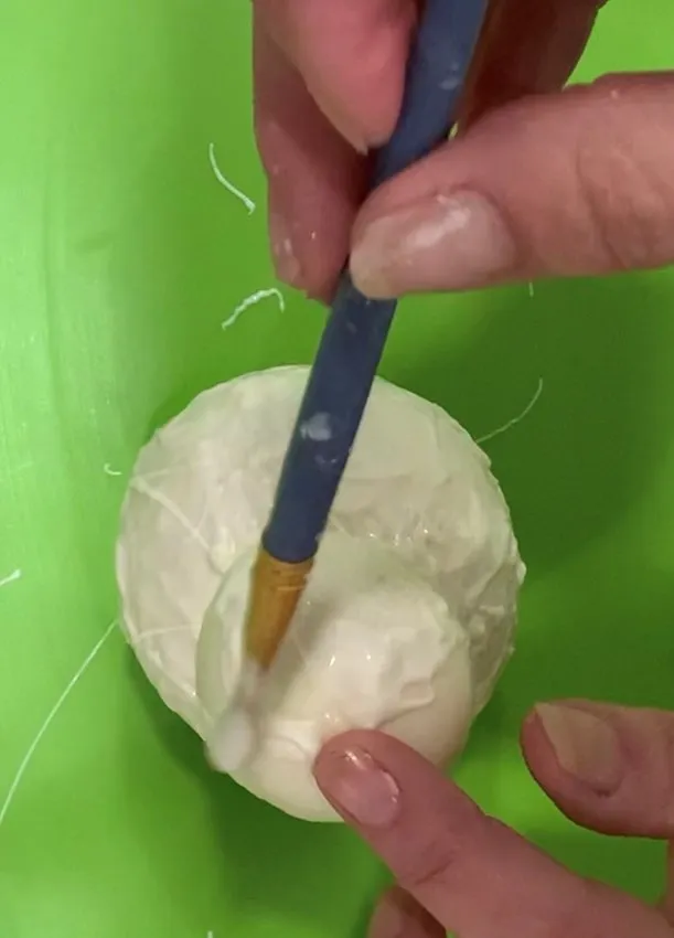 Hand brushing melted white chocolate onto the assembled snowman head.