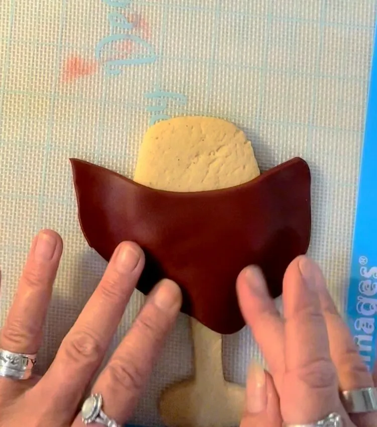 Hand holding a cookie cutter over rolled modeling chocolate for the glass cookie.