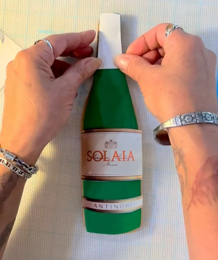 Hands applying an edible label to the modeling chocolate bottle cookie.
