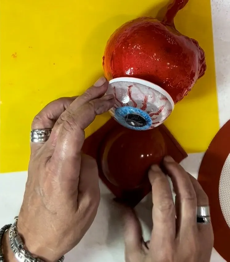 Hands attach the finished isomalt eyeball to the candy apple.