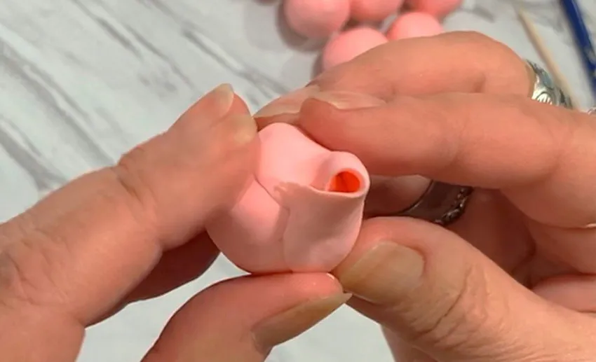 Hand attaching the first modeling chocolate petal to form the rose center.