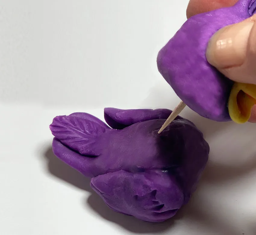 Hand attaching the modeling chocolate head to the body with a toothpick.