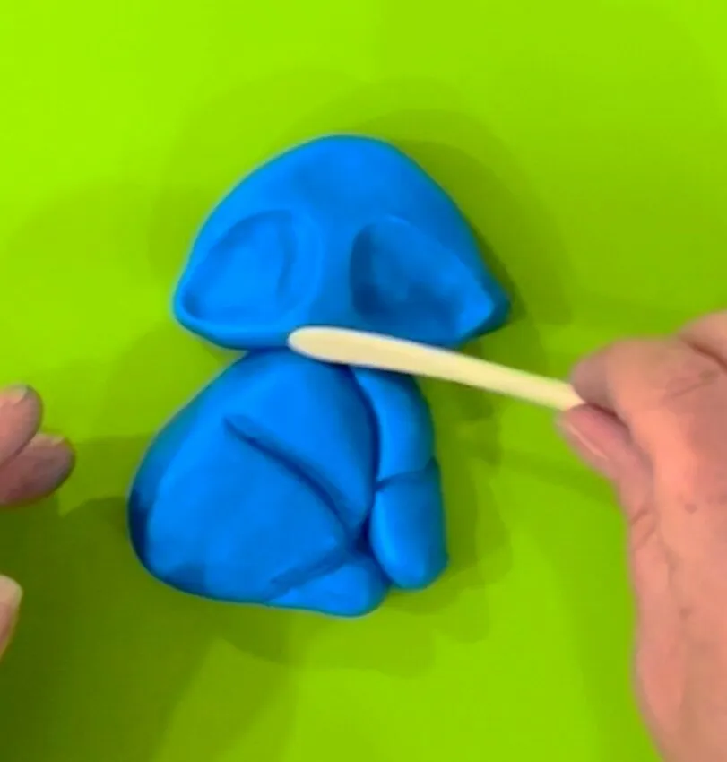Hand using a ball tool to shape the fondant fox head and eye sockets.