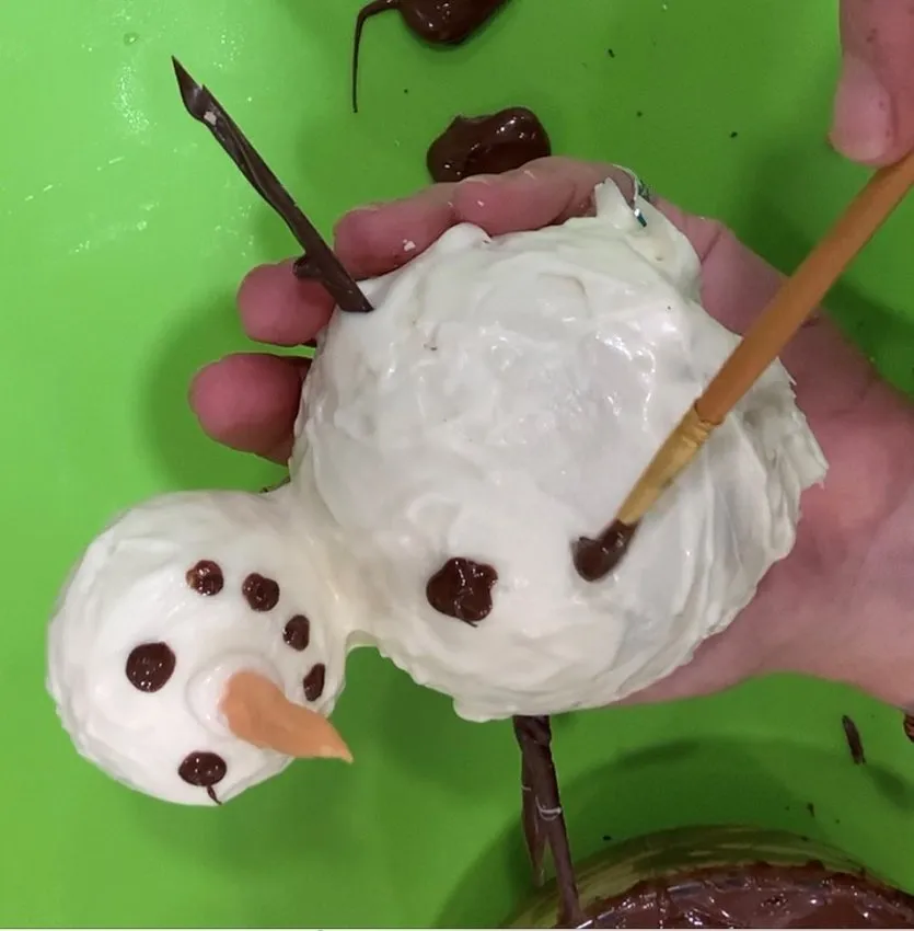Hand painting dark chocolate details onto the snowman body.