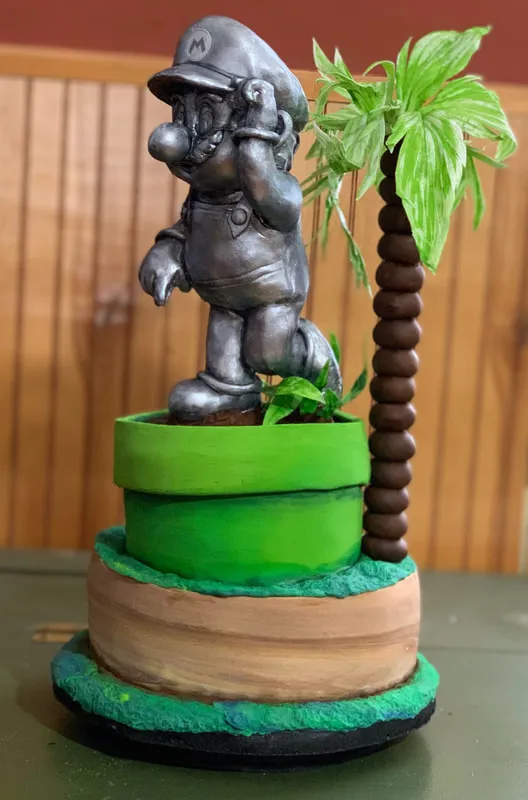 Metallic silver Mario cake with a chocolate palm tree on a tiered base.