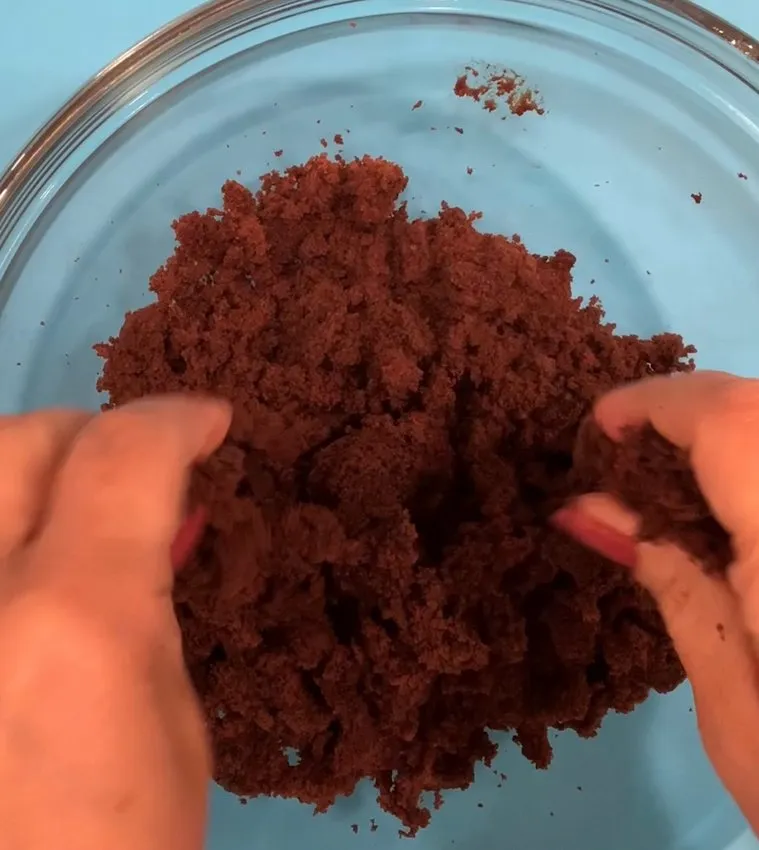 Hands mixing cake crumbs in a glass bowl.