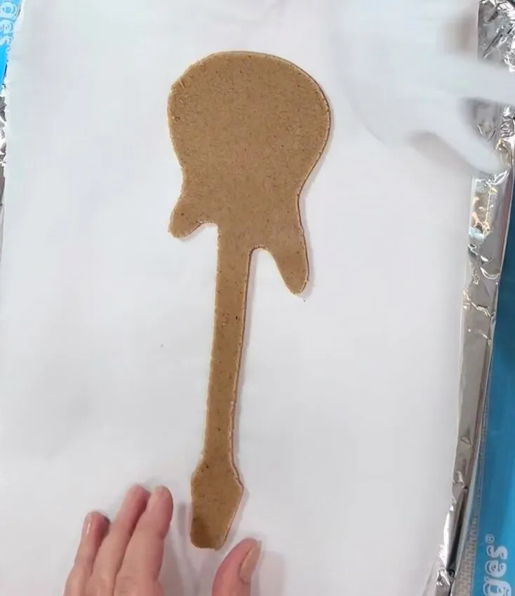 Guitar-shaped cookie cutout on parchment paper before baking.