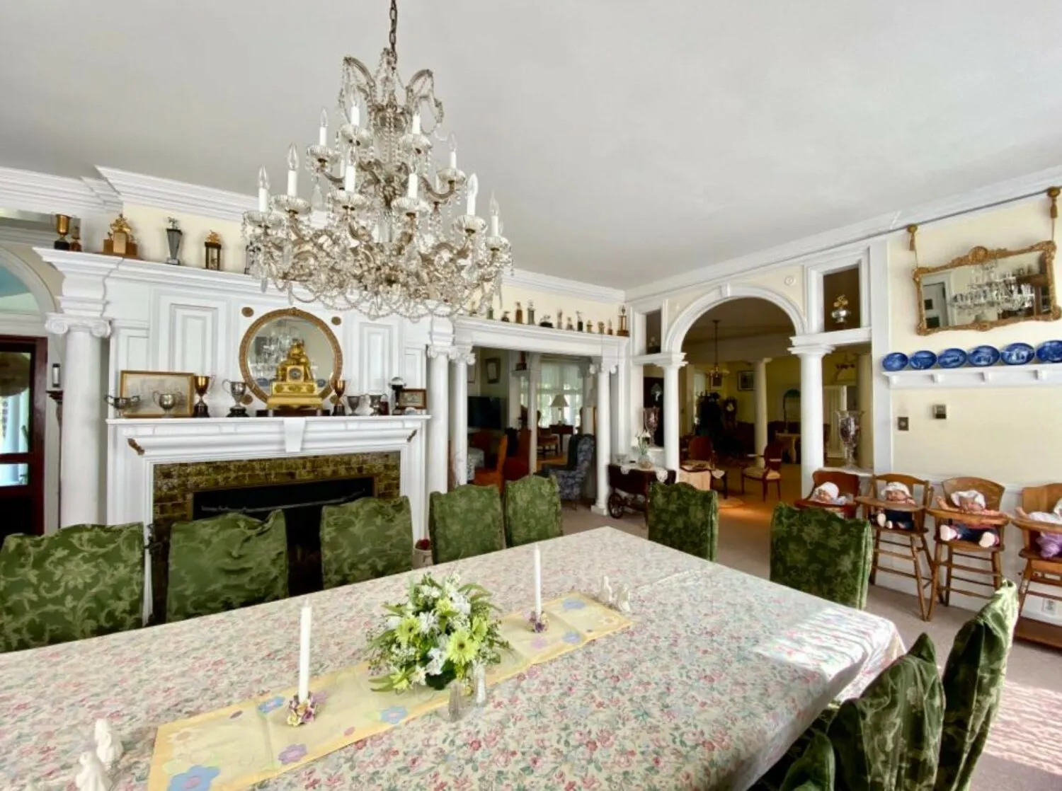 Formal dining room at Burn Brae Mansion with a large table, floral tablecloth, and crystal chandelier.