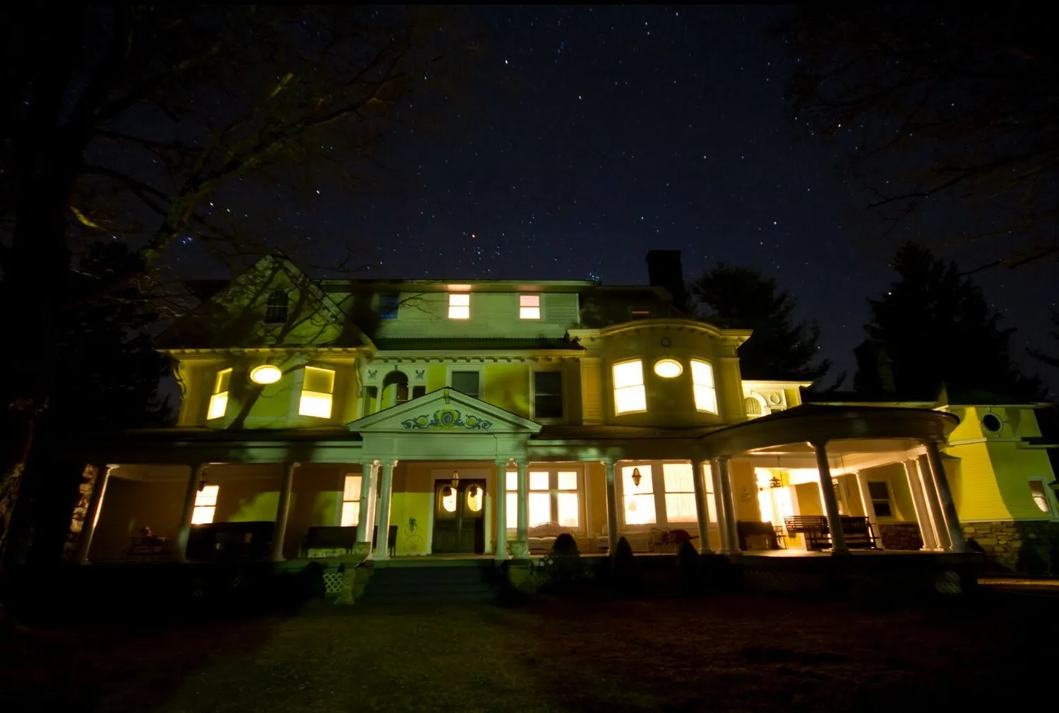 Burn Brae Mansion, a large yellow Victorian house illuminated at night with a wraparound porch.