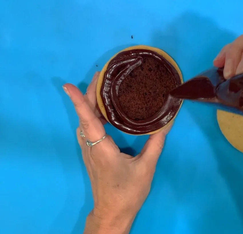 Piping chocolate ganache onto the cookie cake filling.