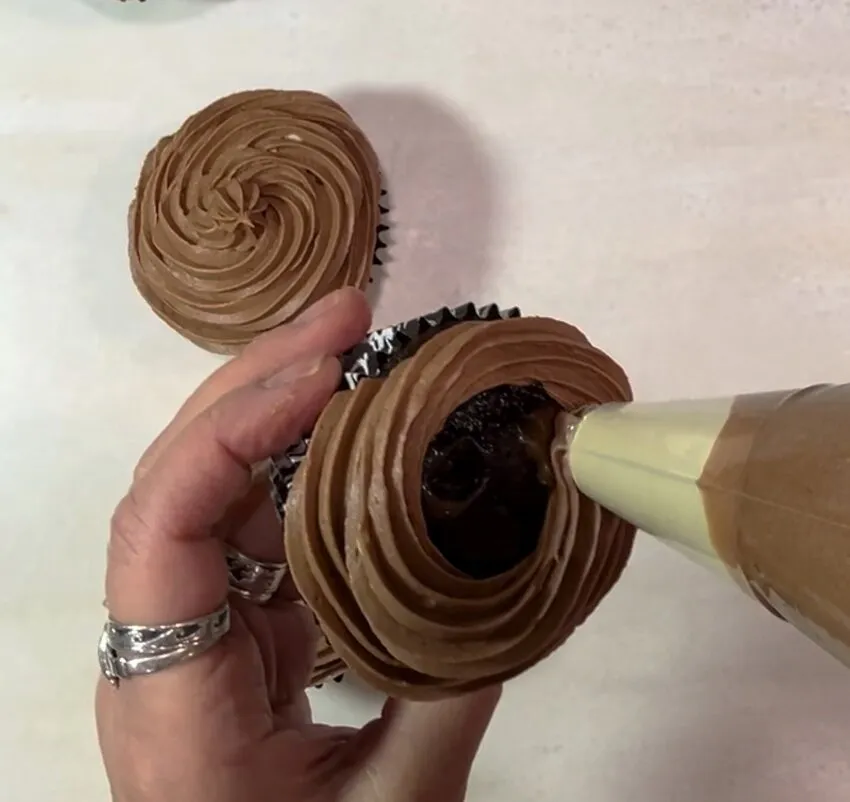 A hand piping chocolate stout buttercream frosting piping bag onto a cupcake in a black-and-white patterned liner