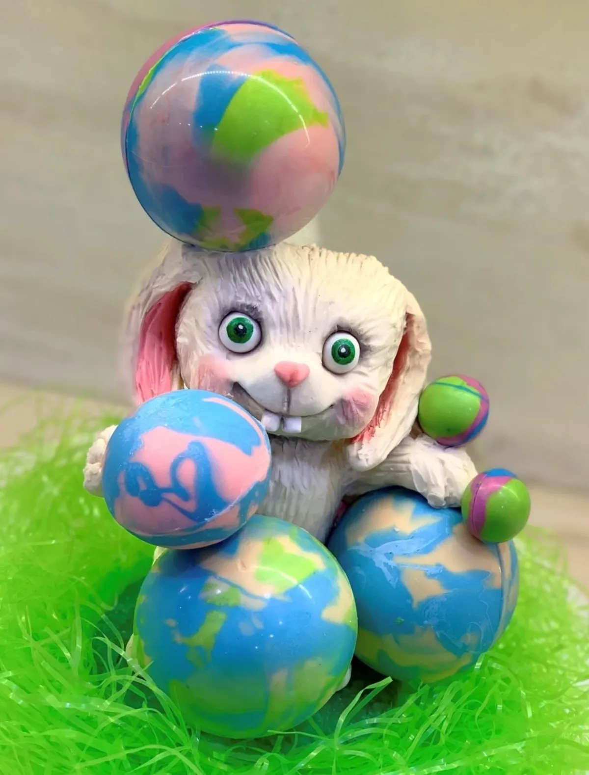 A white fondant bunny figurine with large green eyes amidst colorful Easter eggs