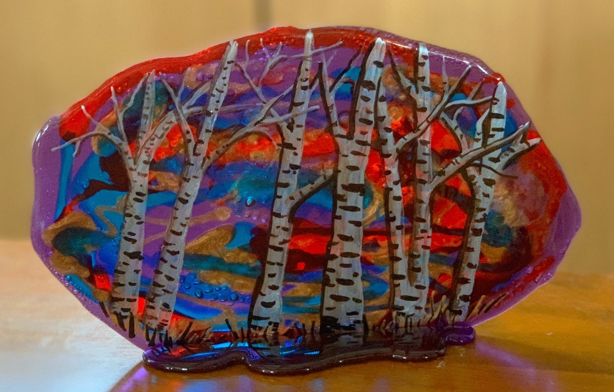 A handcrafted sugar fused glass art piece featuring white birch trees with black markings set against a vibrant, abstract background of red, purple, and blue hues.