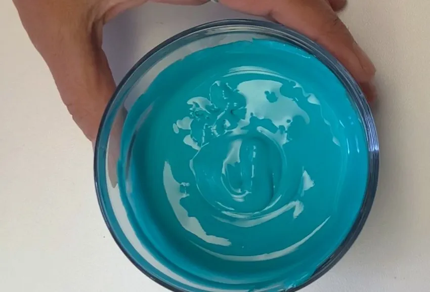 Checking consistency of turquoise royal icing in a glass bowl