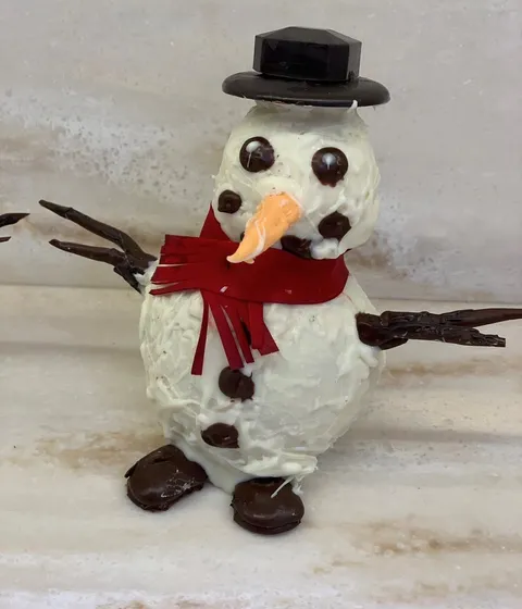 A chocolate snowman dessert with frosting, chocolate chip buttons, and a scarf