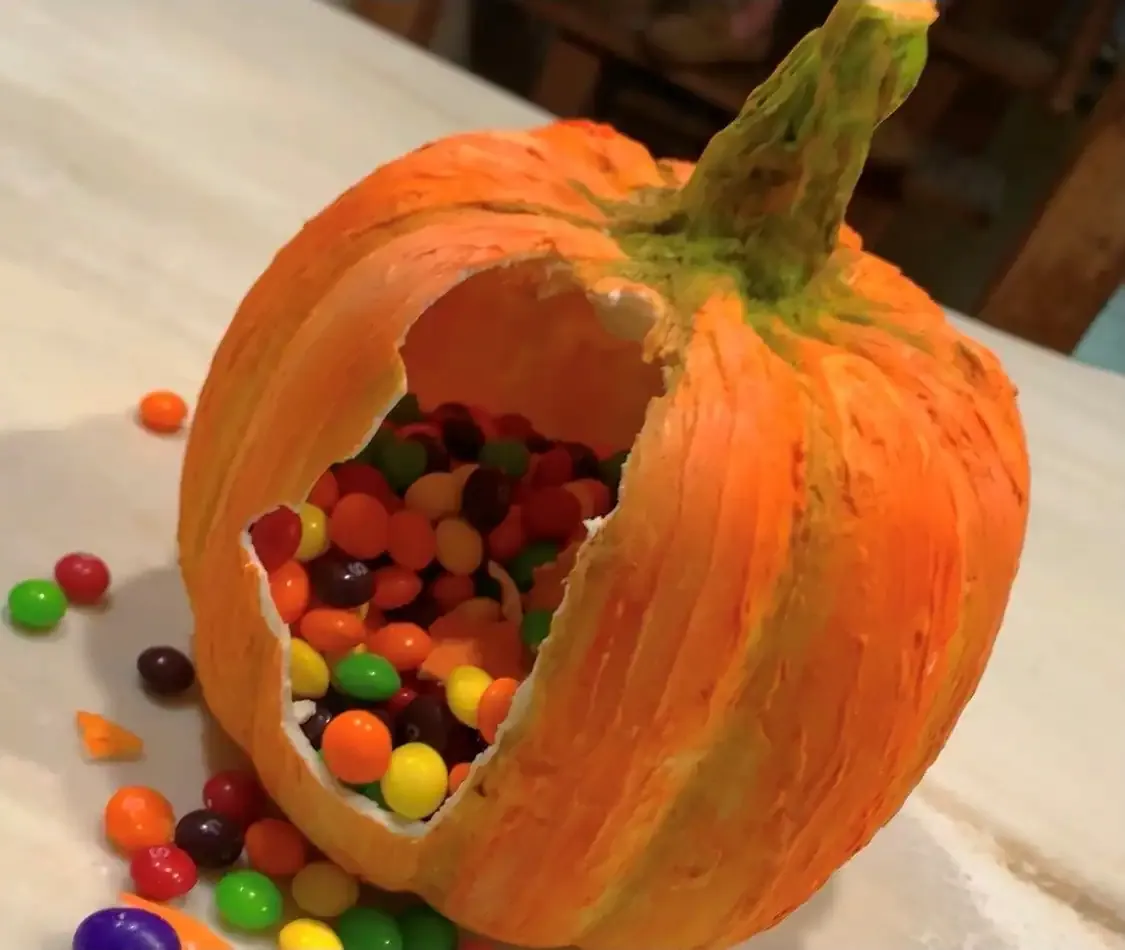 A hollow chocolate pumpkin filled with colorful candies on a white surface