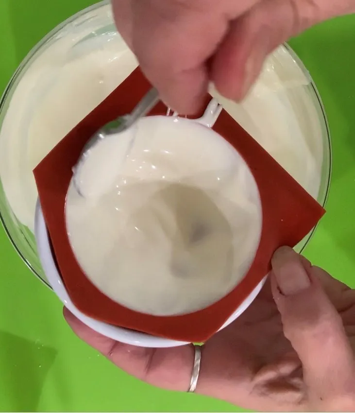 Spoon spreading melted white chocolate inside a silicone mold.