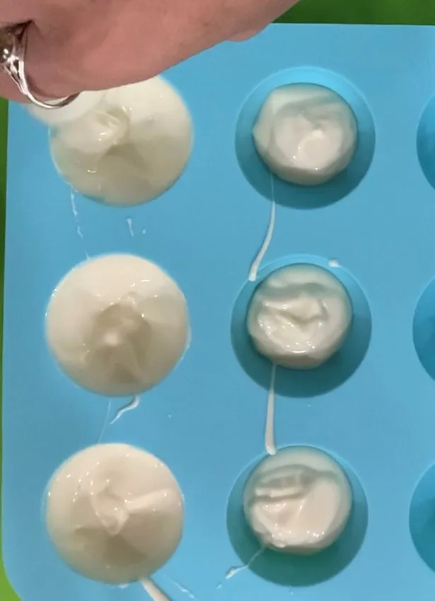 Hand pouring white chocolate into small half-sphere silicone molds.