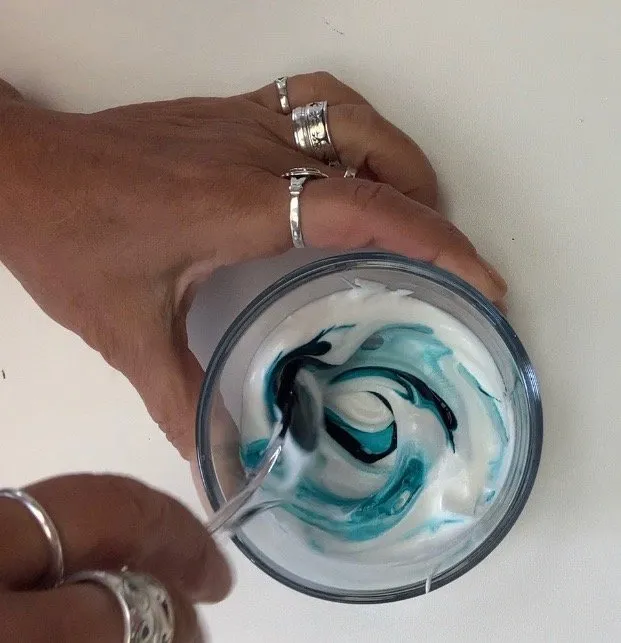 Bowl of white icing being mixed with blue gel color