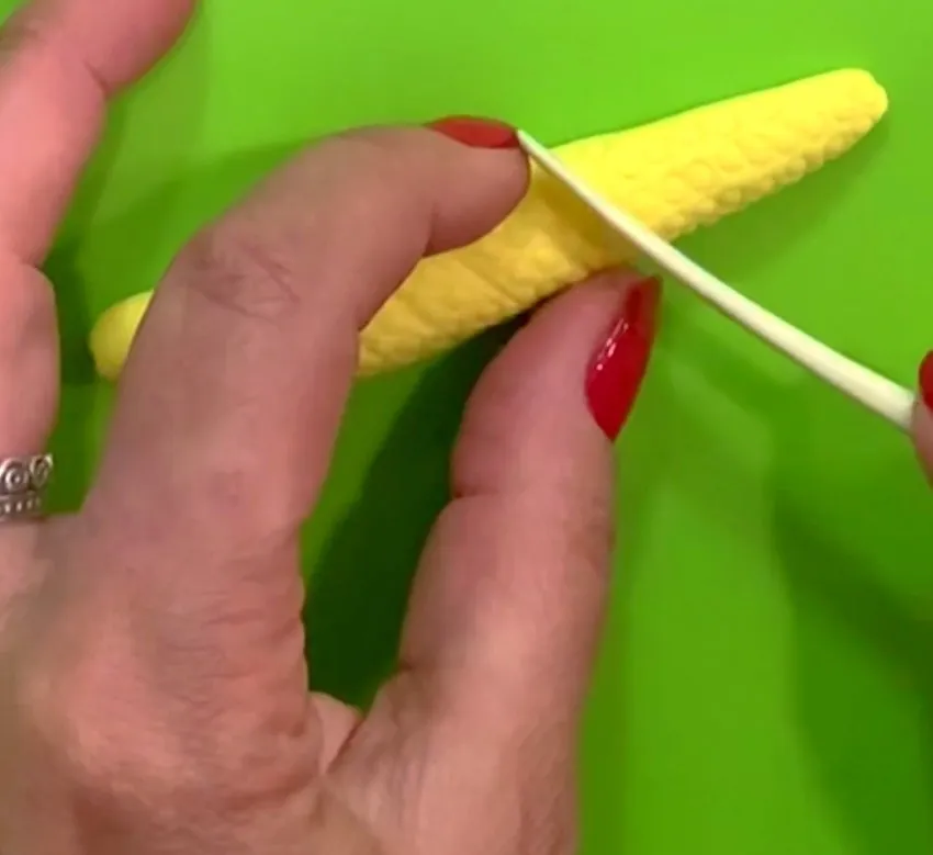 Hand texturing a yellow fondant corn cob with a wooden stick.