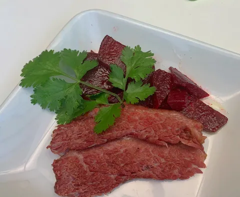 Sliced corned beef brisket arranged on a white plate, garnished with fresh herbs