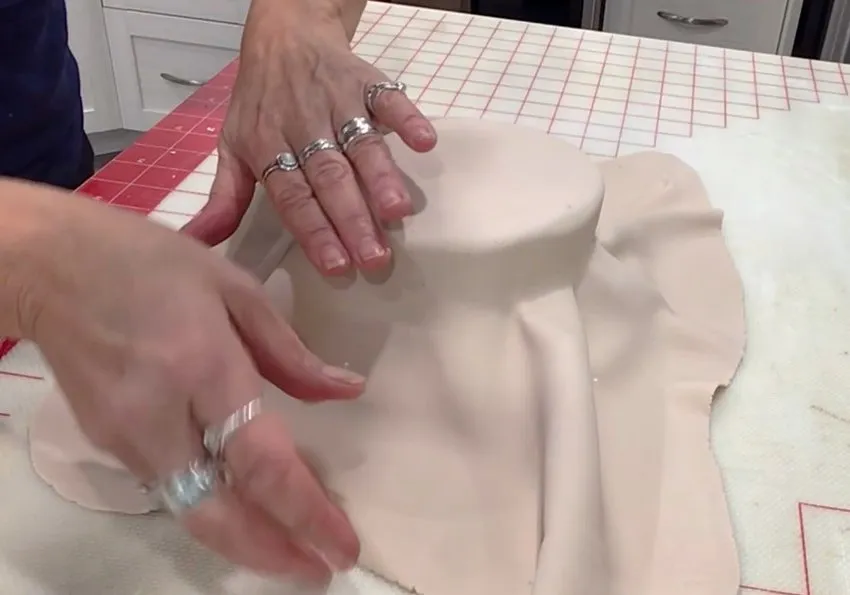 Hands cover the bottom bun cake layer with rolled beige fondant.