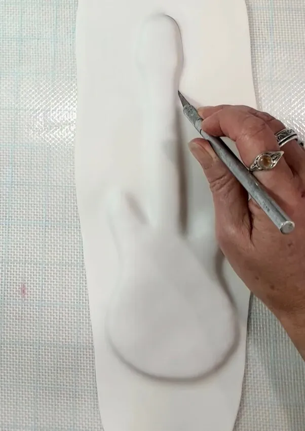 Hand cutting fondant around a guitar-shaped cookie with a knife.