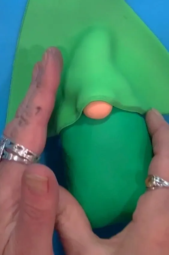 Hands press green fondant to cover the gnome hat shape.
