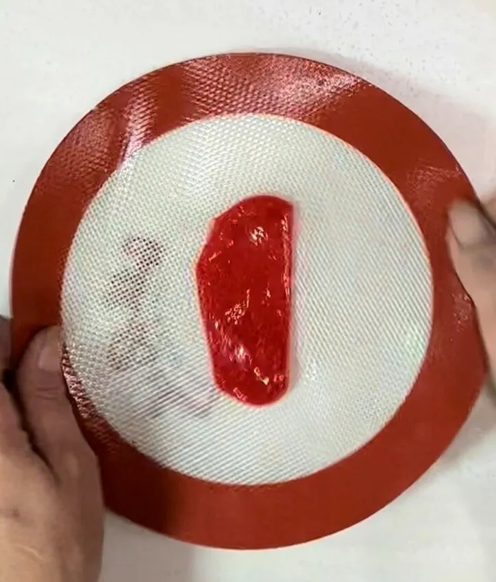Hands manipulate melted candy on a silicone mat to form a stem shape.