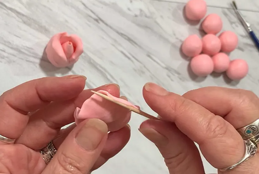 Hand using a toothpick to curve the edges of a modeling chocolate petal.
