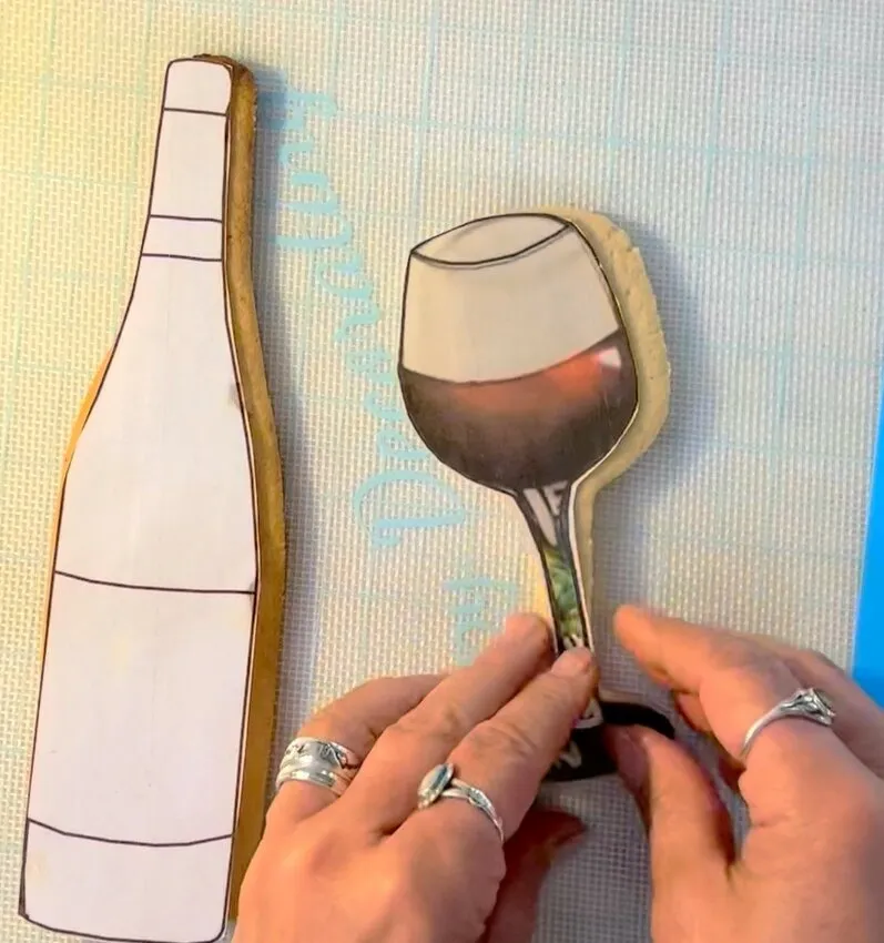 Baked wine bottle and wine glass shaped cookies on a mat.