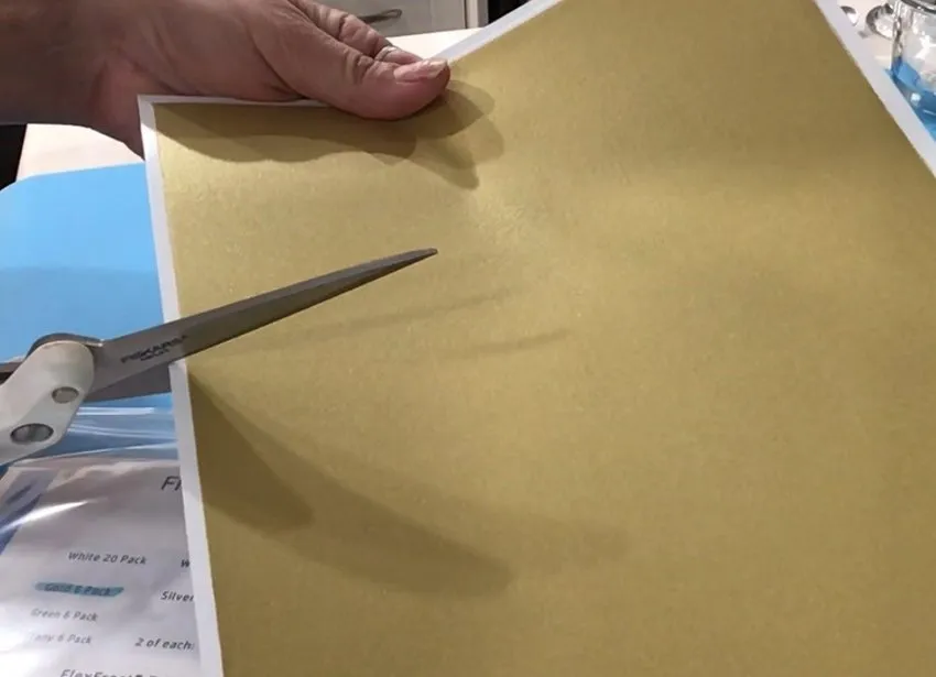 Scissors cutting a white edible lace fabric sheet.