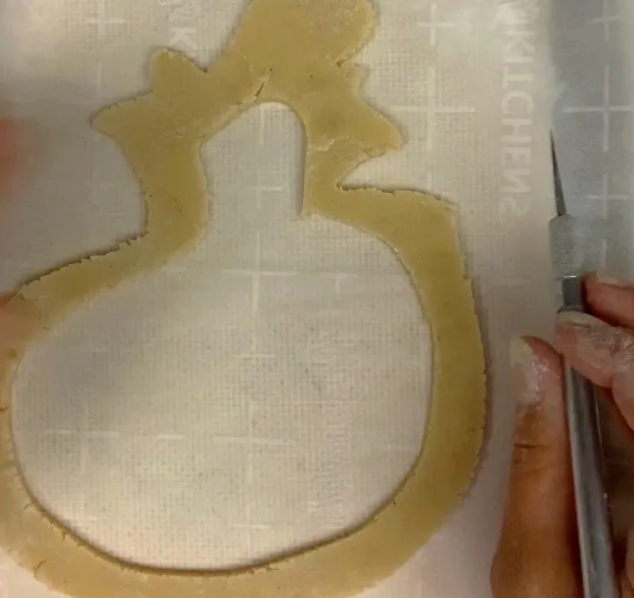 A hand cuts the inner border of a Halloween cookie shape with a precision knife.