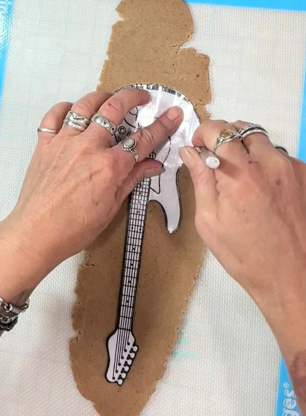 Hands pressing a guitar stencil onto rolled cookie dough.