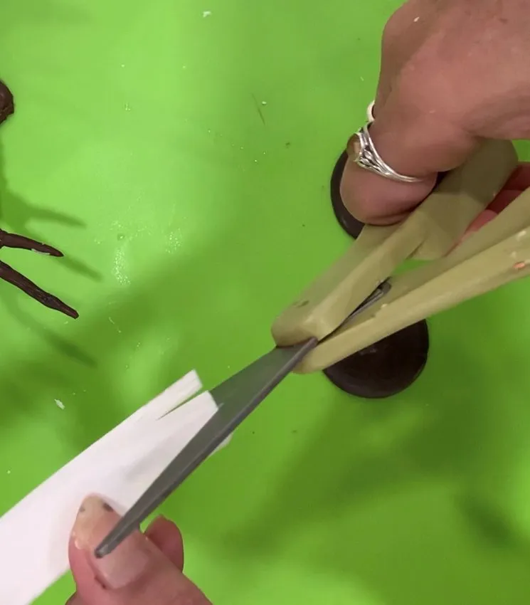 Hands cutting a strip of edible paper for the snowman scarf.