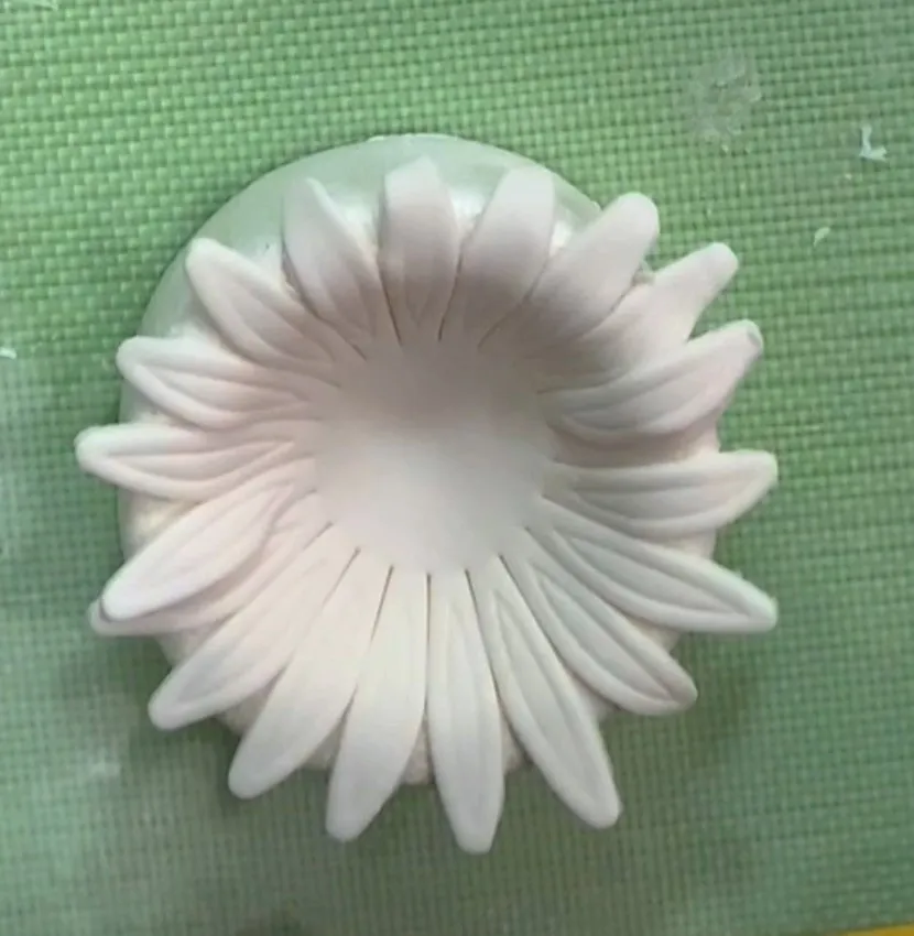 Cut gumpaste sunflower shape on a green silicone mat.