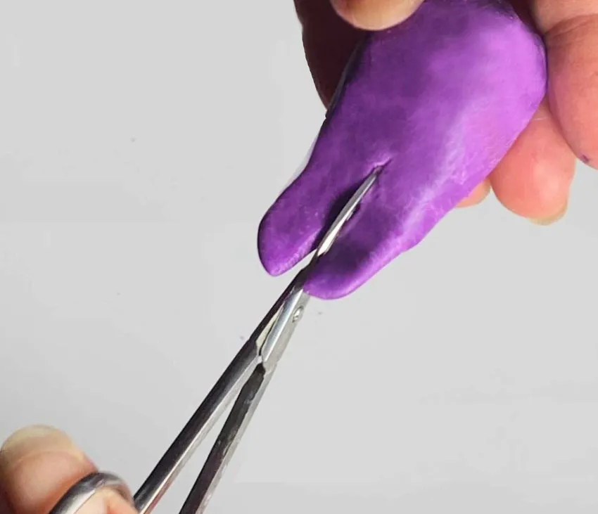 Hands cutting a tail slit in purple modeling chocolate body with scissors.