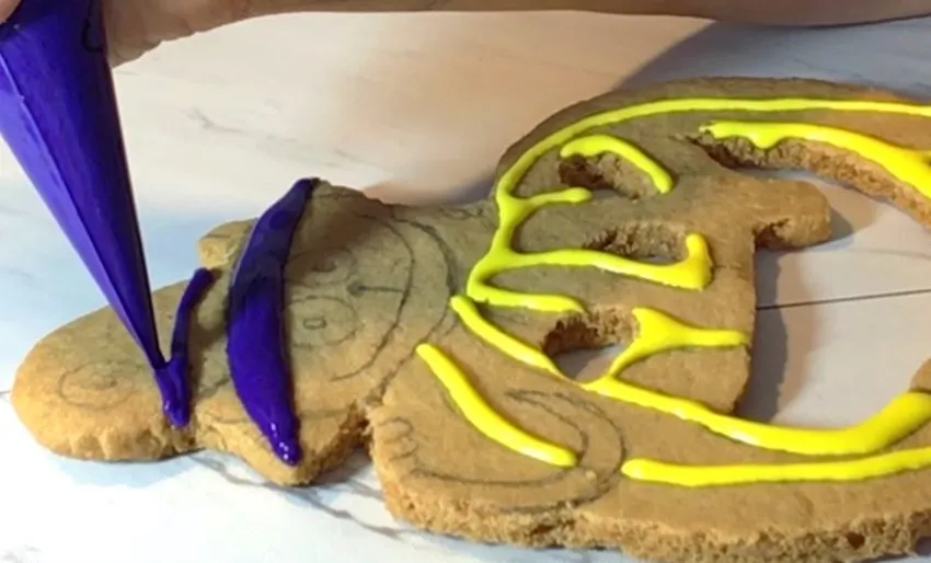 A hand pipes royal icing onto the Halloween top cookie.