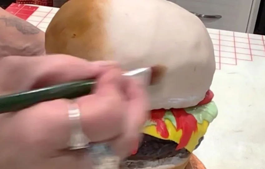A paintbrush applies brown edible color detail to the top bun.