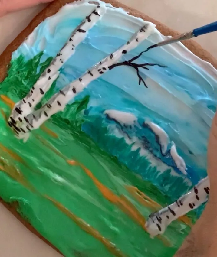 Hand adding black royal icing branch details to the birch trees.