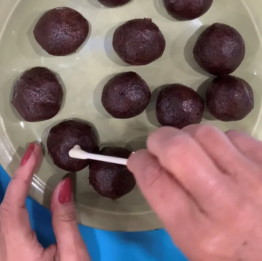 Hands inserting lollipop sticks into cake balls.