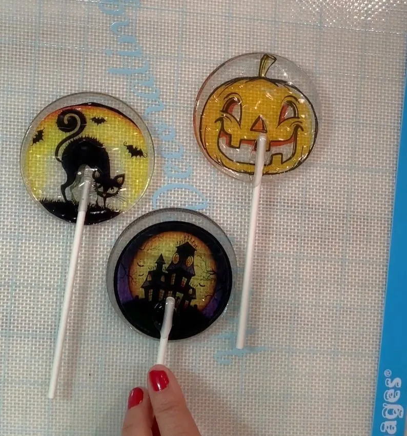 Three finished Halloween isomalt lollipops resting on a silicone mat.