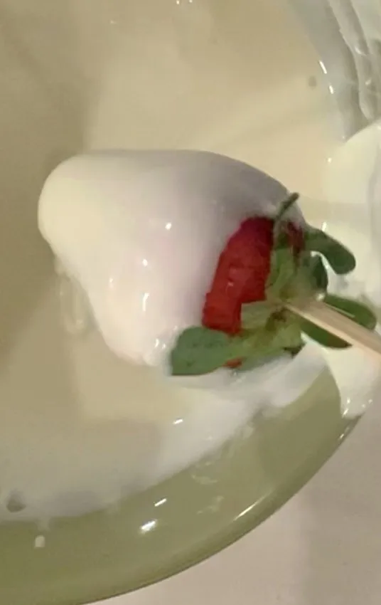 Strawberry being dipped into melted white chocolate