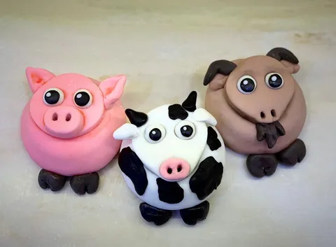 Three fondant-decorated cupcakes designed as a pig, cow, and sheep farm animals