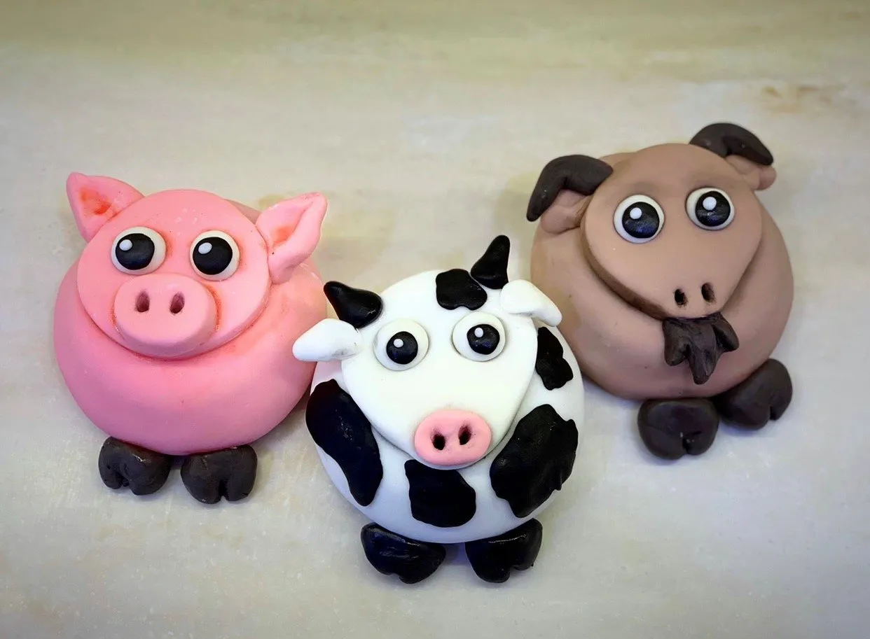 Three fondant-decorated cupcakes designed as a pig, cow, and sheep farm animals