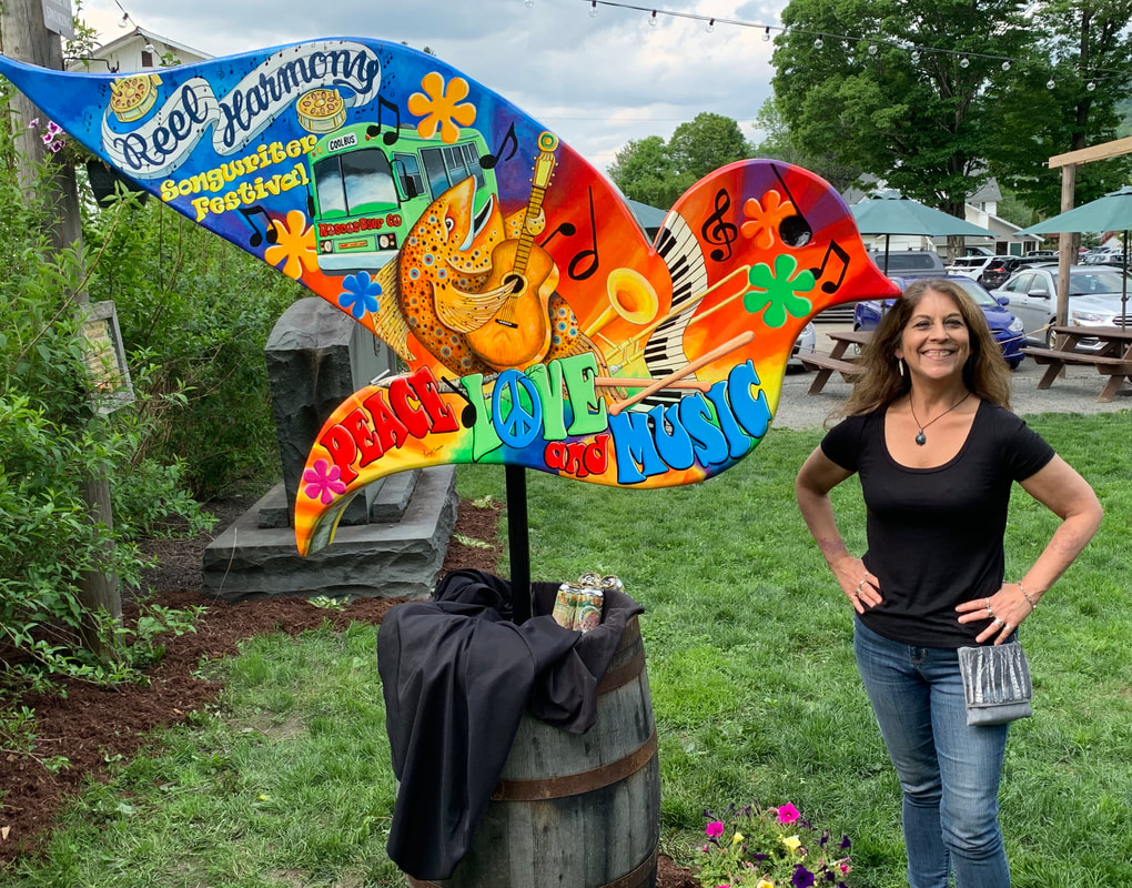 A colorful, psychedelic wooden bird sculpture painted with peace signs, flowers, and the word "LIBERTY" in bold letters, set against a vibrant red background.
